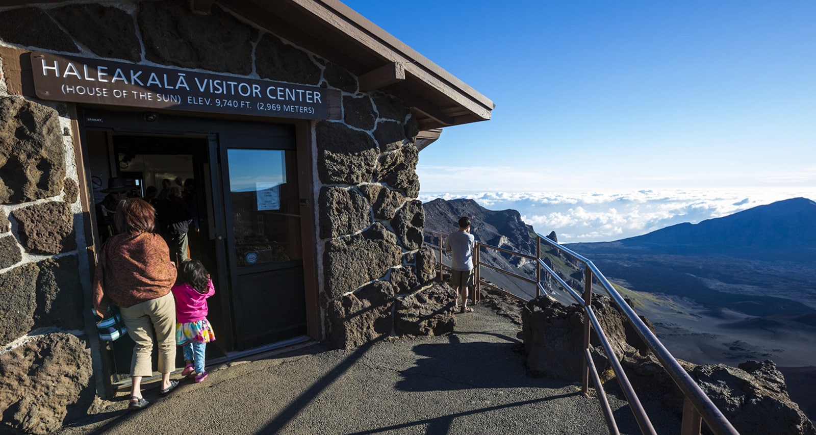 People enter a stone structure located at the top of a rugged hillside