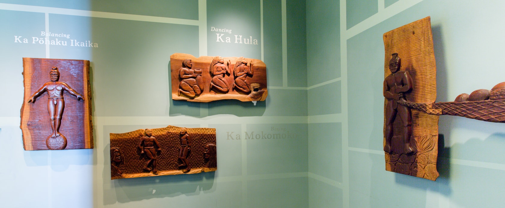 先住民のさまざまな動作を表現した木のレリーフ、その説明を簡潔に示すハワイ語のフレーズと英語の翻訳
