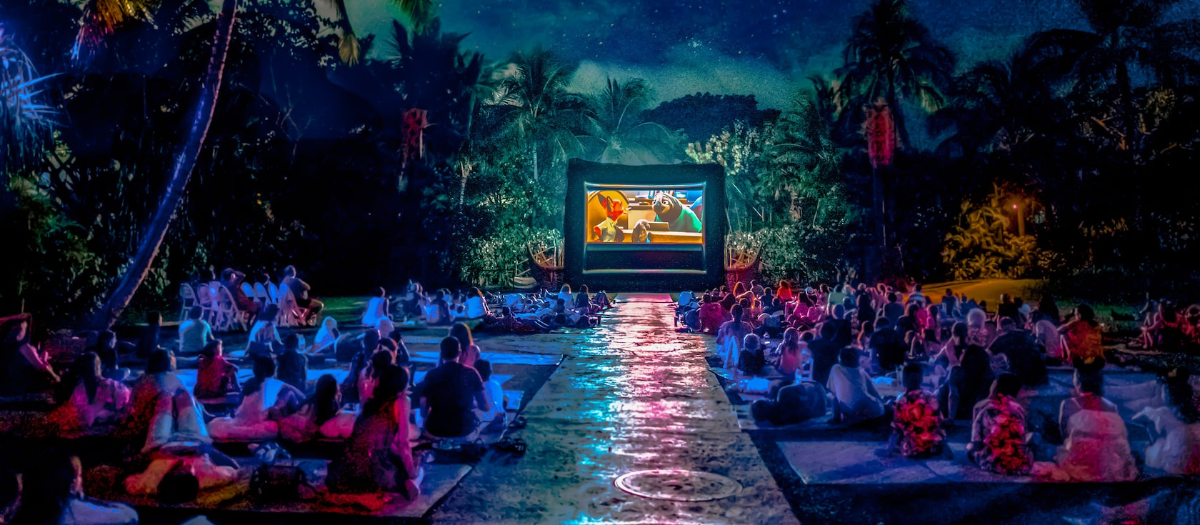 Guests seated on a large lawn, watching a movie screening after dark