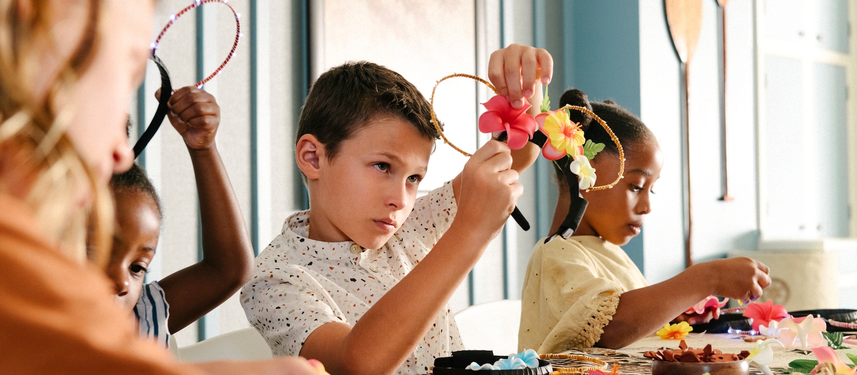 テーブルに座り、花と他の材料を組み合わせてミッキーの耳の形をしたヘッドバンドを作っている子供たち