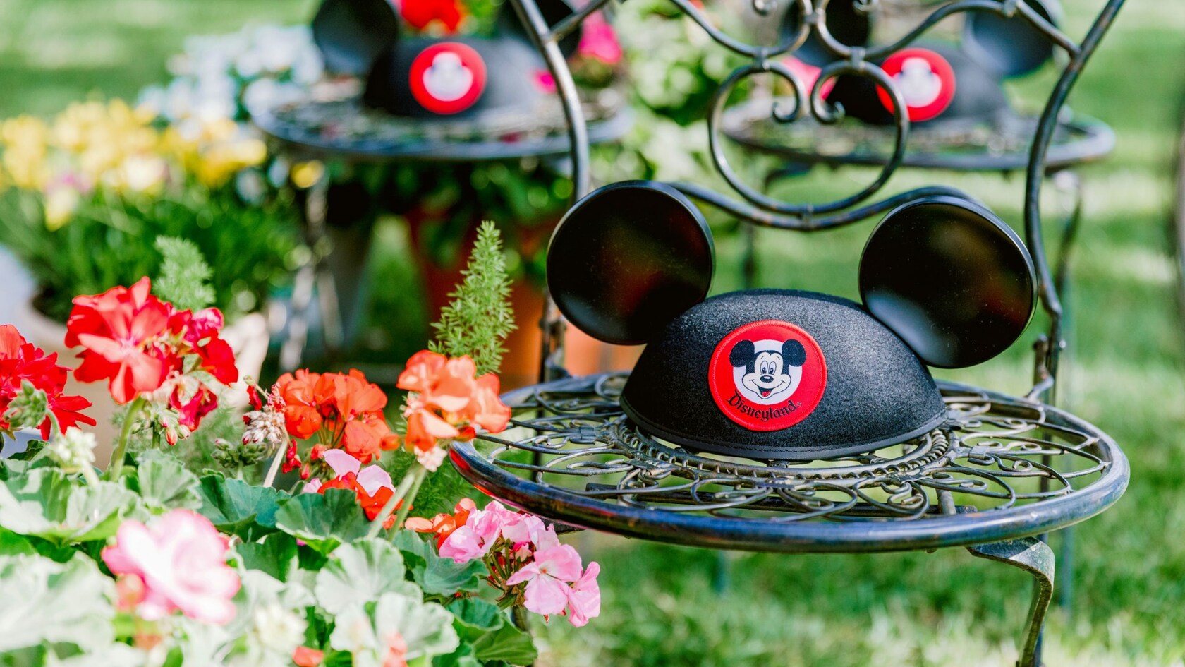 Tres sillas de hierro forjado en un jardín, cada una con un sombrero con orejas de Mickey Mouse en el asiento