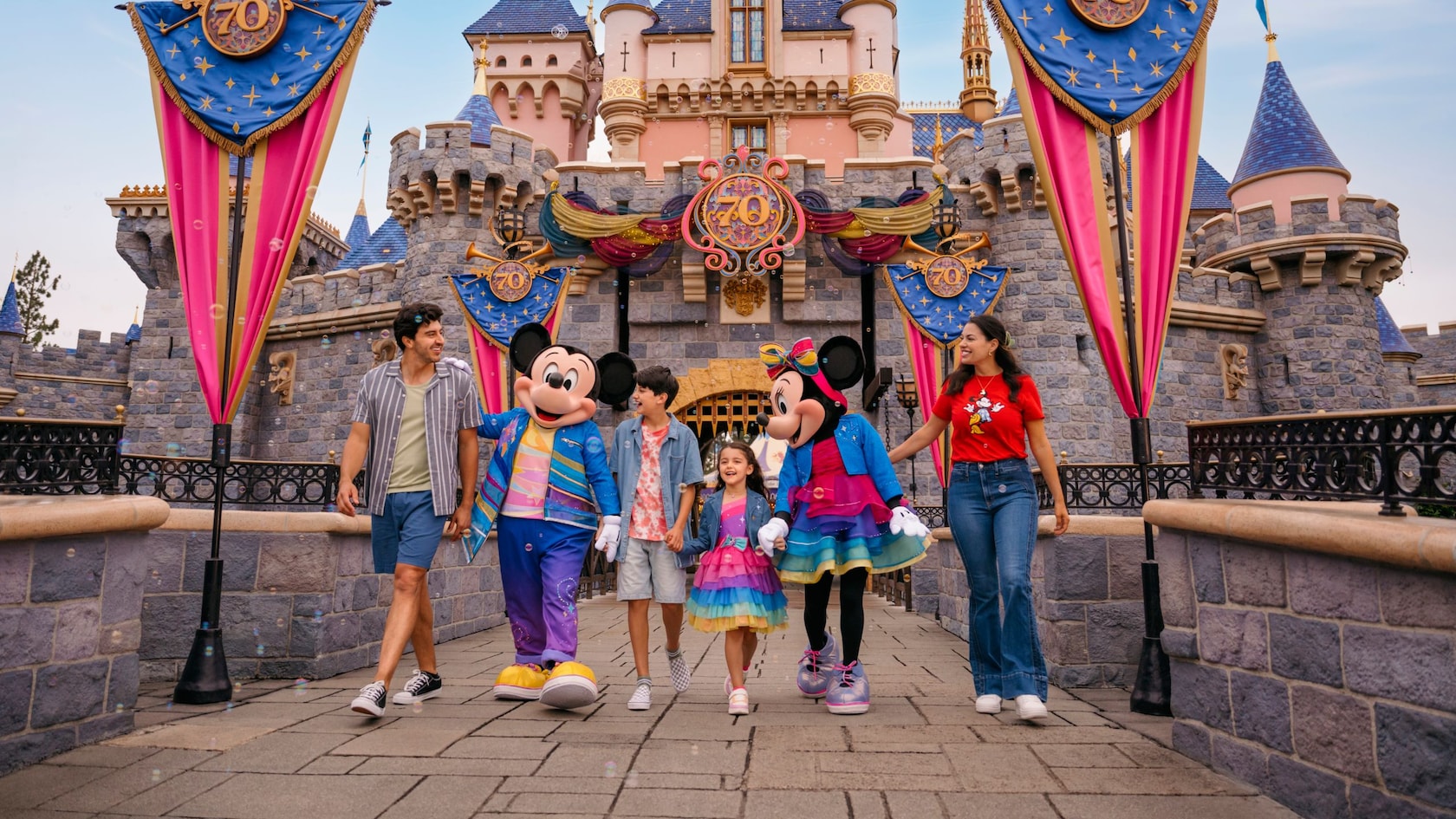 Familia caminando con Mickey y Minnie Mouse frente al castillo de Disneyland durante la Celebración del 70.º Aniversario