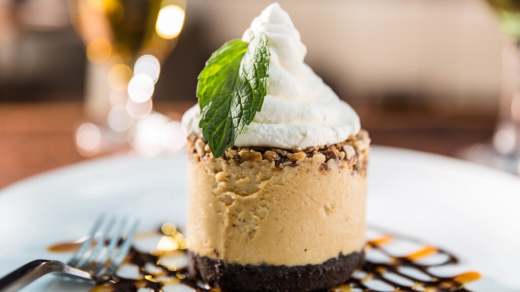 A torta de pasta de amendoim Snickers coberta com chantili e um ramo de hortelã em um prato regado com calda de chocolate e caramelo