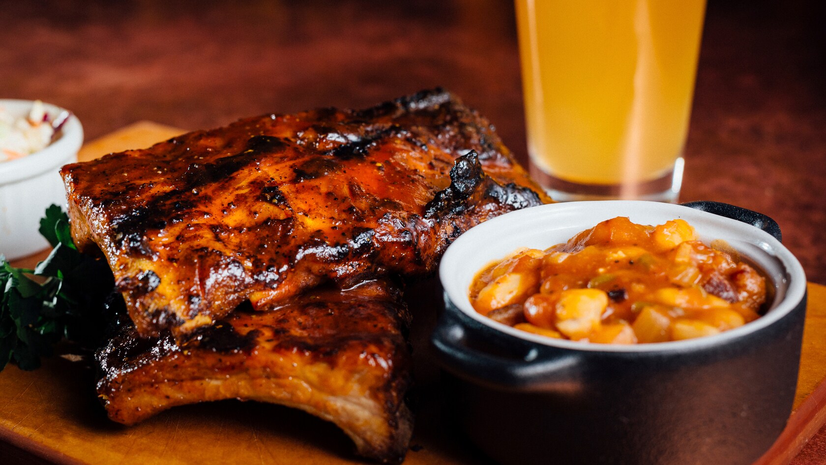 Costelinha ao molho barbecue com feijão assado e creme de milho em pratos estilo caçarola e copo de chope