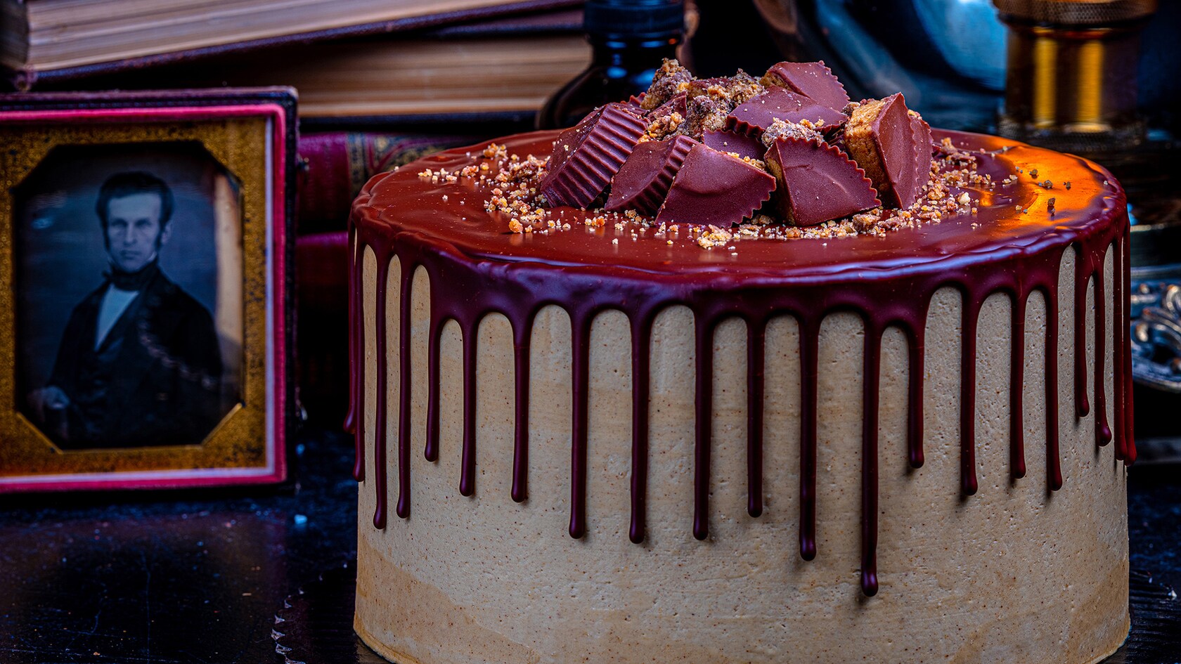 A Peanut Butter Cake topped with chunks of Peanut Butter Cups with chocolate ganache pouring over the sides