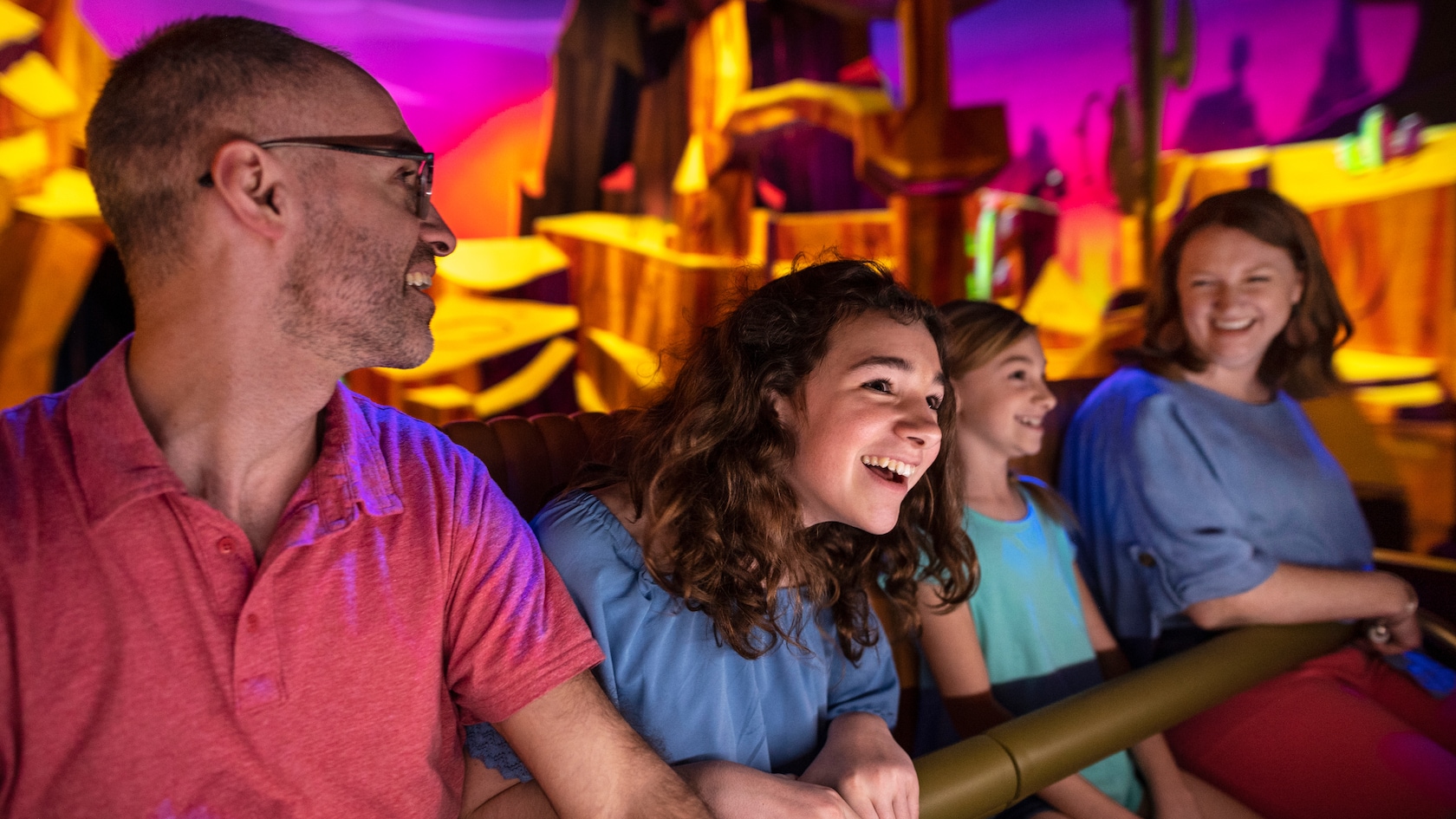 A father, mother and their two daughters seated in an attraction vehicle