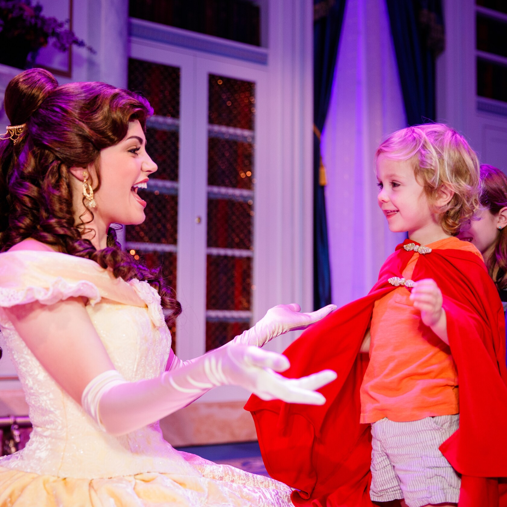 Belle kneels down to a hug a child wearing a cape