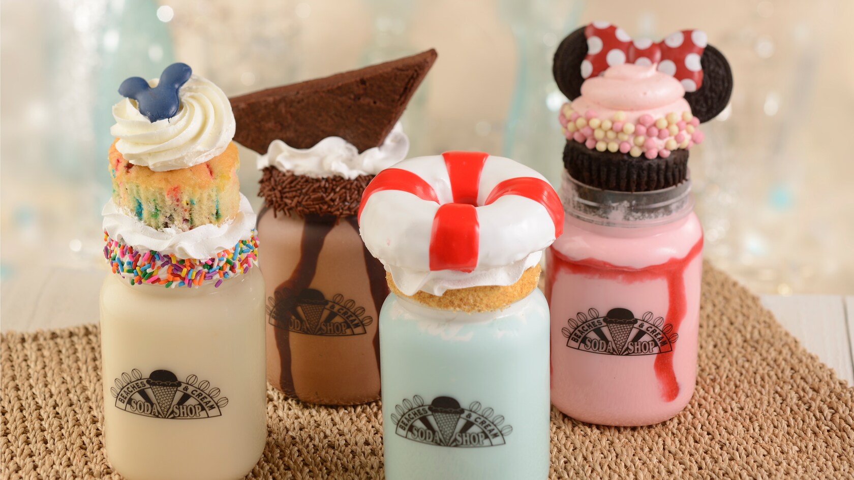 Milkshakes served in mason jars and topped with small cupcakes and other desserts