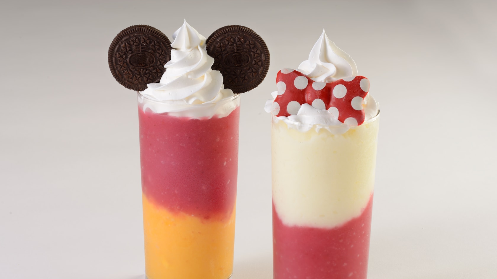 Frozen Mickey Smoothie featuring whipped cream and Oreo cookies next to a frozen Minnie Smoothie featuring whipped cream and a white chocolate bow