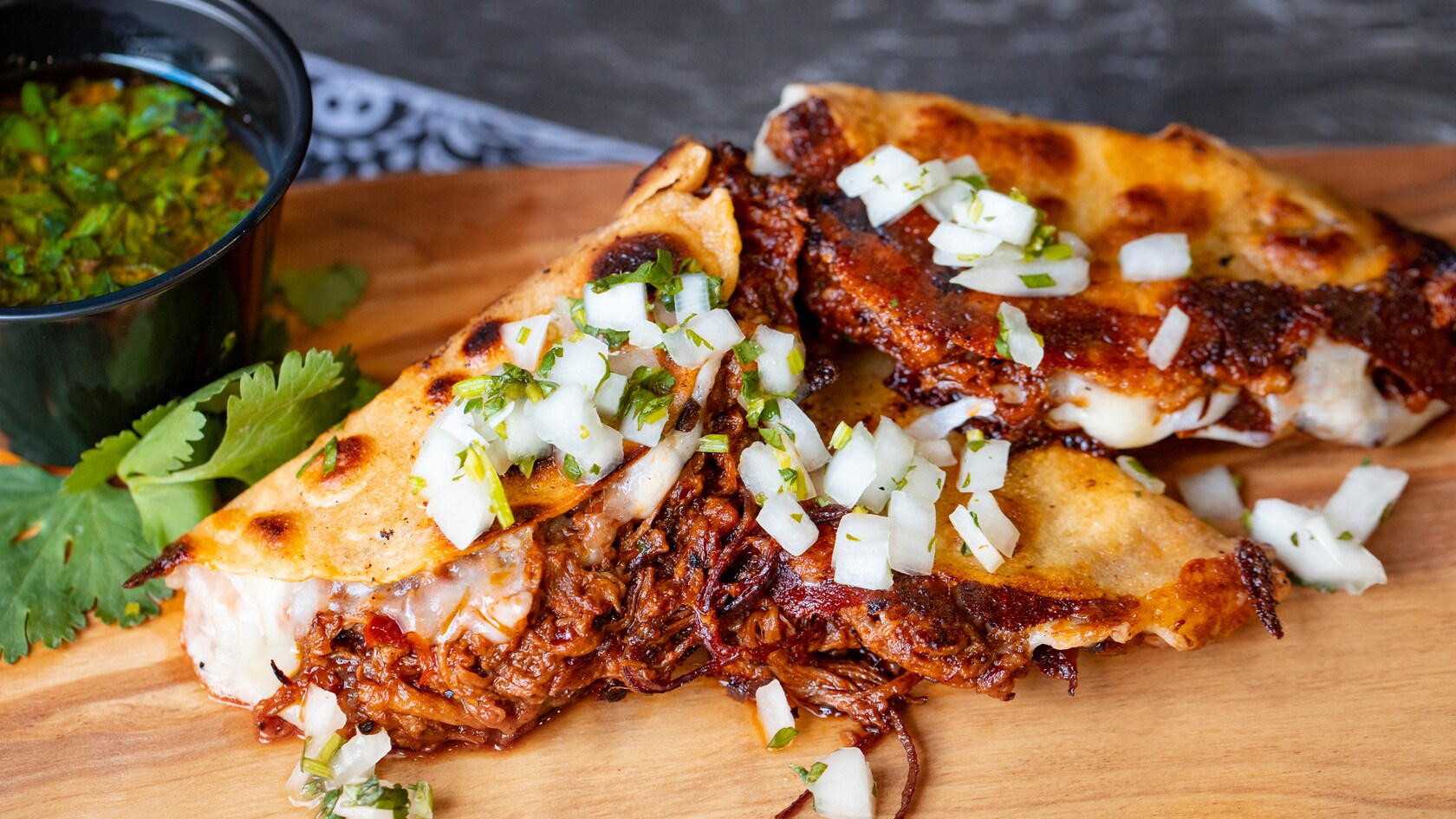 Um mix de carne bovina em uma casquinha de taco com cebola, salsinha e coentro, servido em uma travessa de madeira