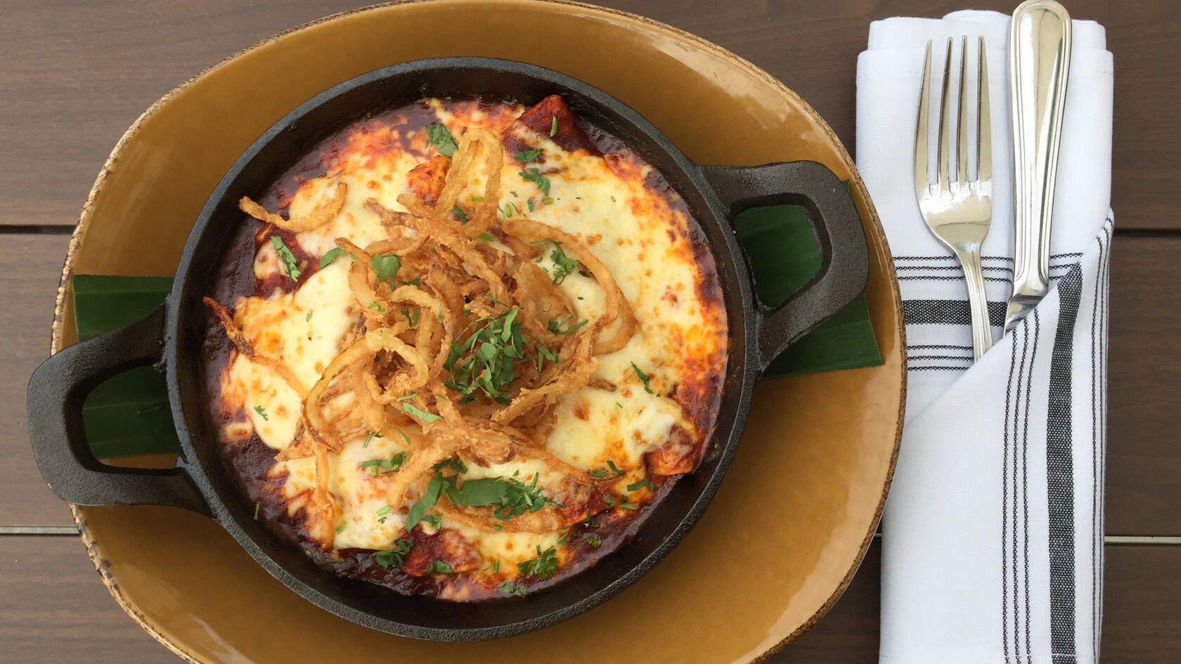 Enchiladas served in a cast iron dish and topped with melted cheese, crispy onion and cilantro