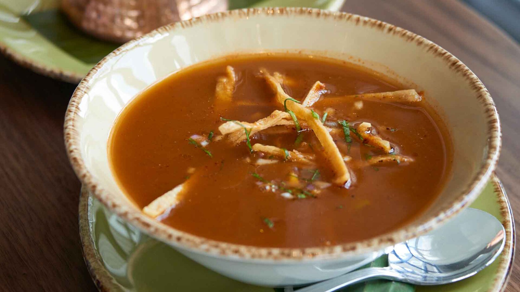 A bowl of tortilla soup topped with chicken, avocado, cheese, onion, cilantro and tortilla chips