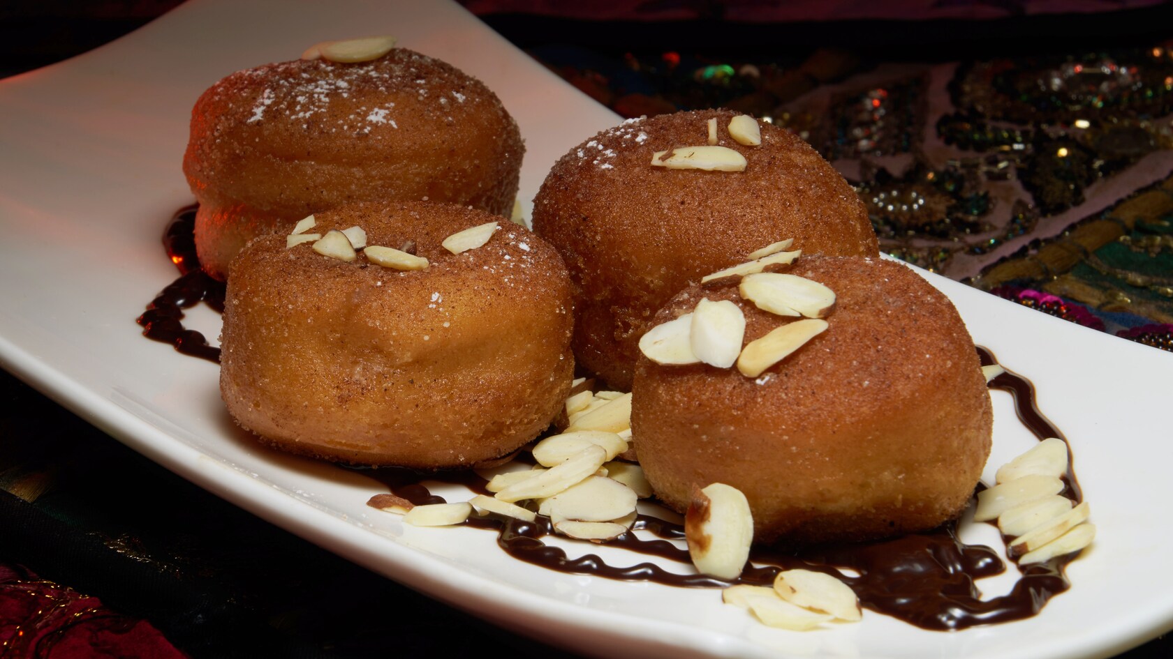 4 puffy, deep fried pastries topped with almond slices and garnished with a drizzle of chocolaty sauce