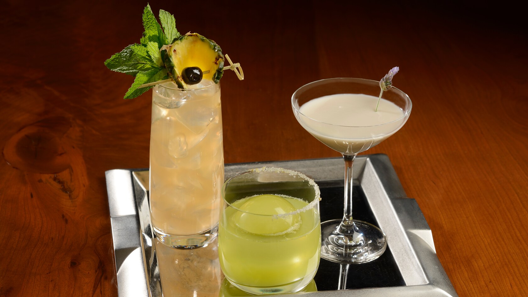 Three specialty cocktails being served on a tray