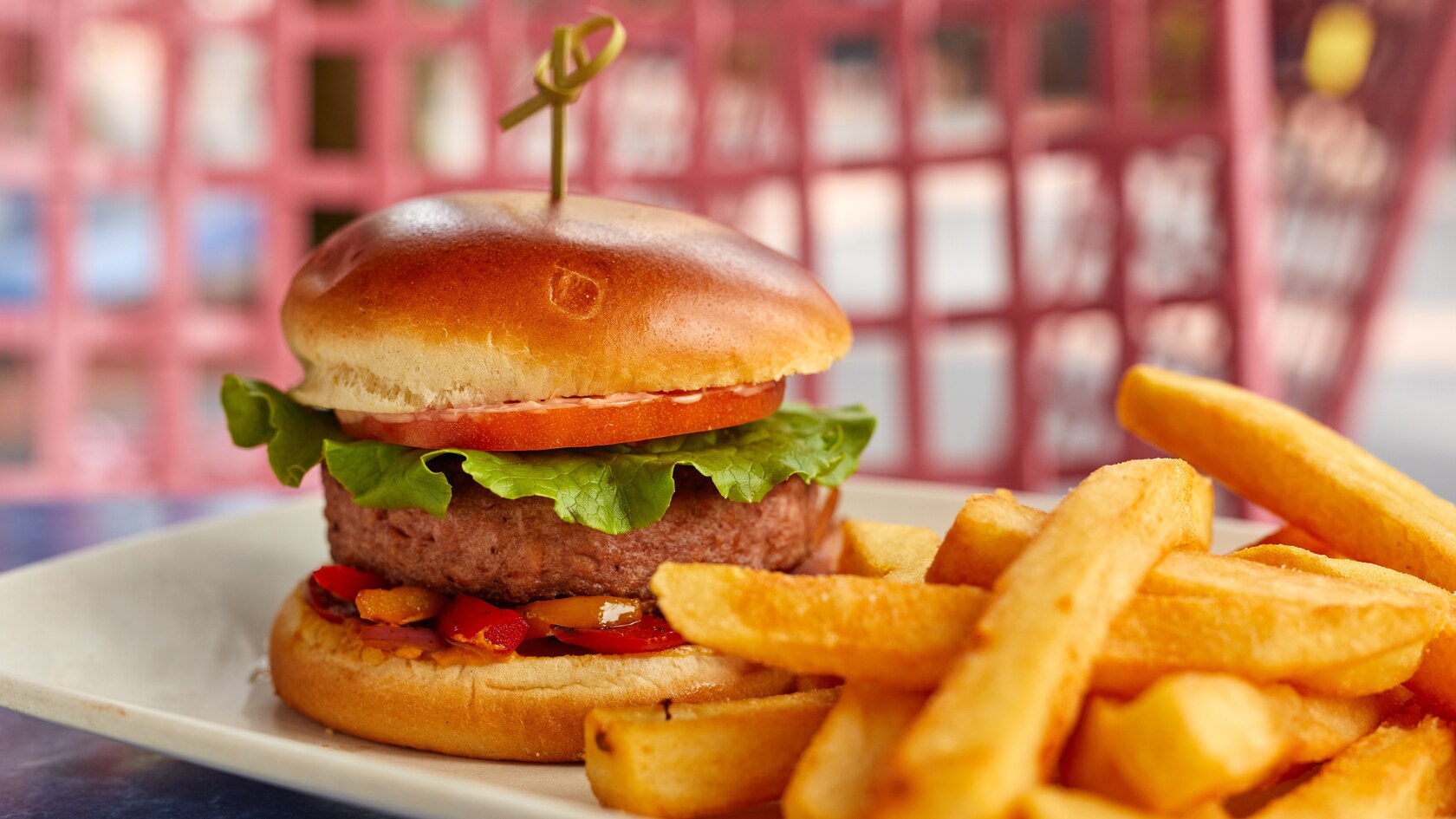 Una hamburguesa con lechuga, salsa, tomate y más en un panecillo, servida al plato con papas fritas
