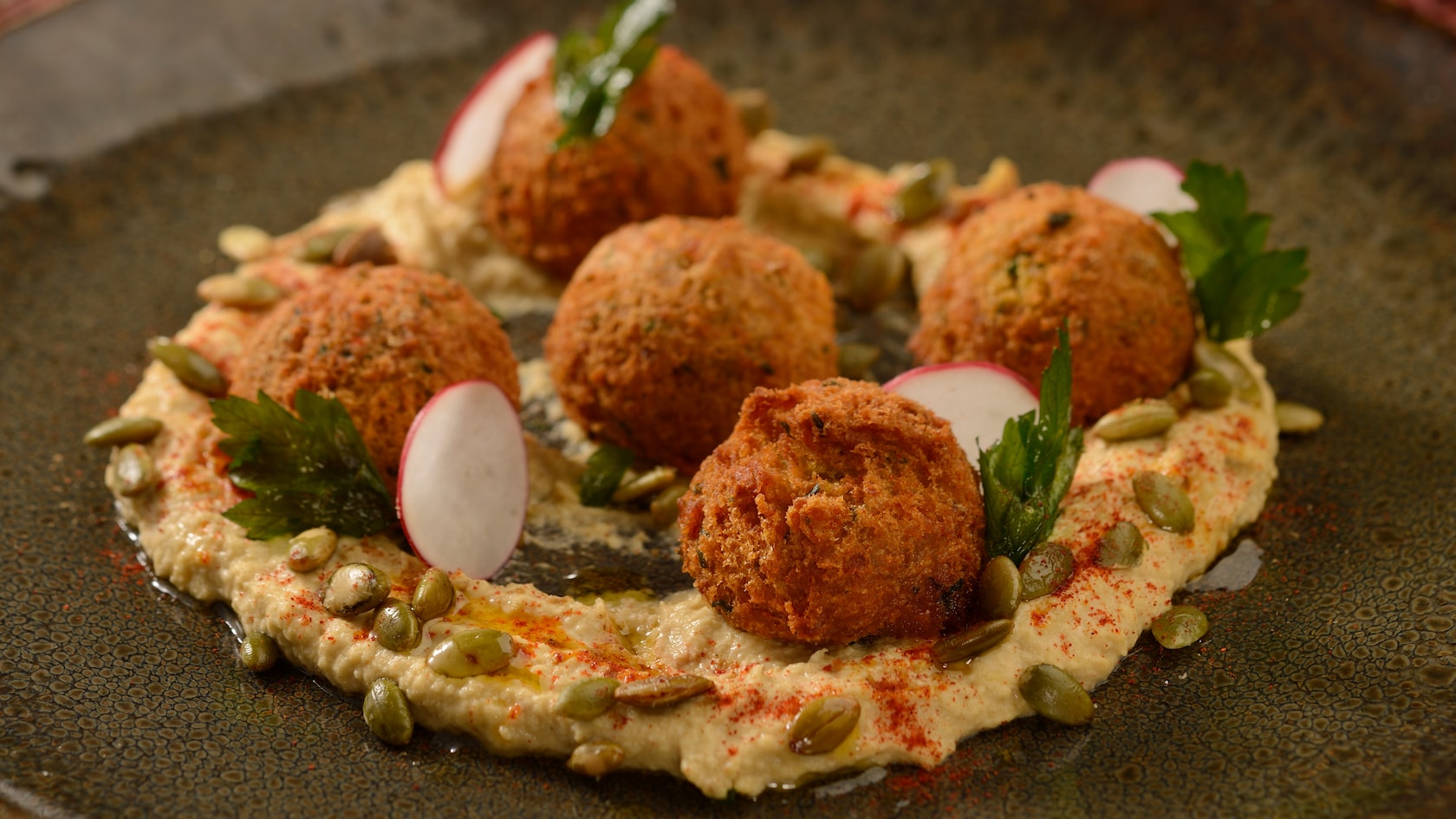 A dish of falafel on top of hummus with sliced radishes and pine nuts