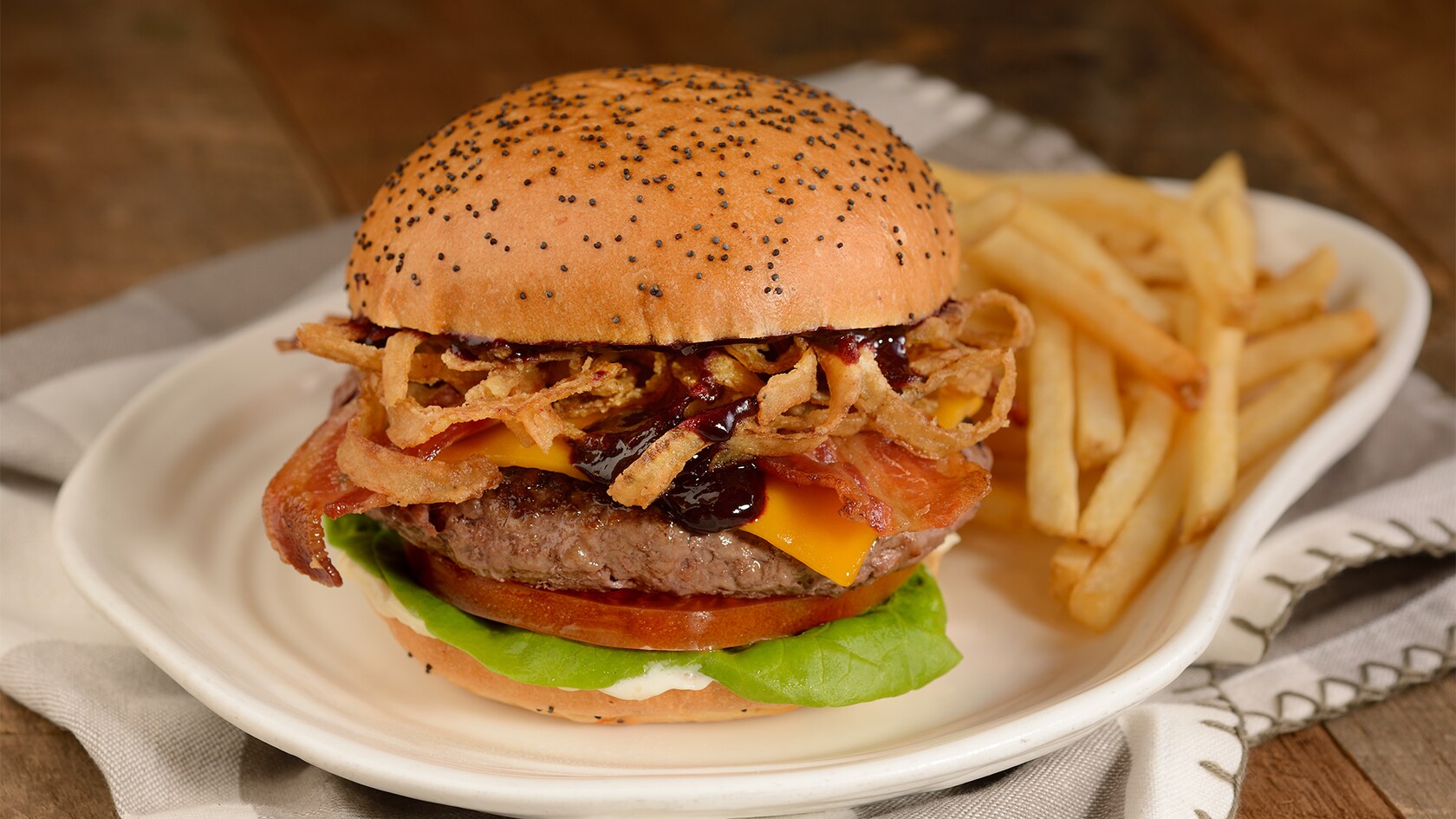 A hamburger topped with pieces of lobster, thermidor sauce and crispy Parmesan cheese, served with french fries
