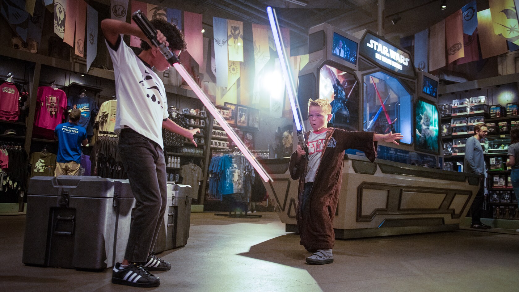 Amidst store displays, 2 young boys pretend to battle with lightsabers