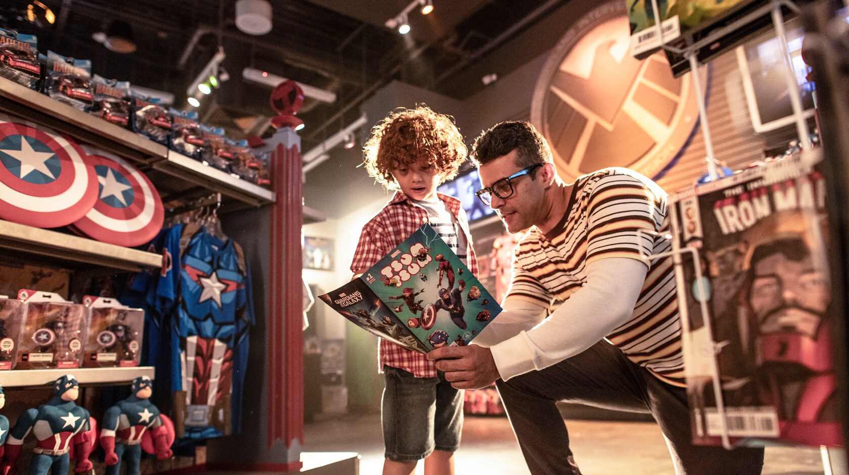 Un jeune garçon et son père lisent une bande dessinée parmi des produits Capitaine America et Iron Man