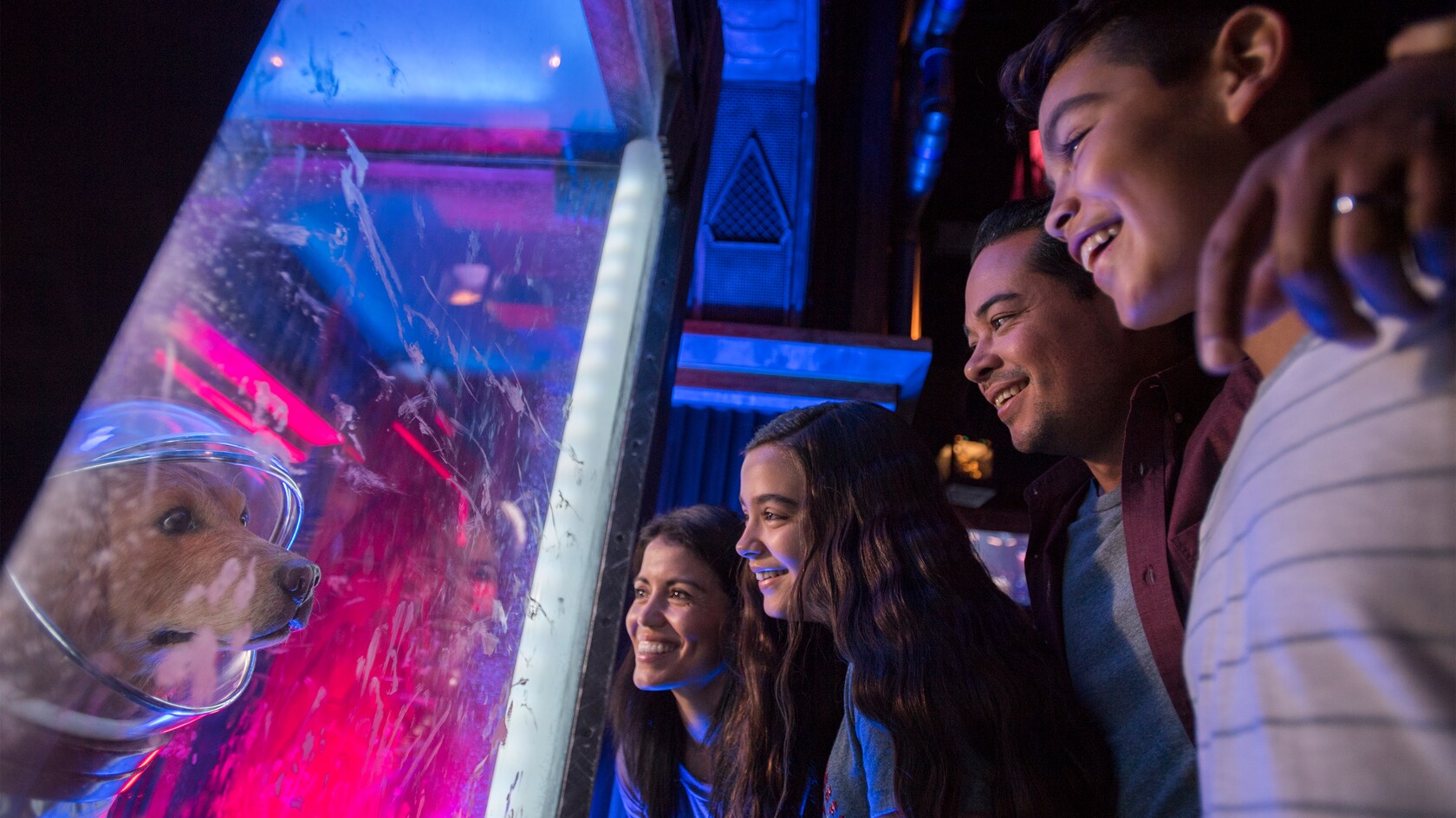 Guests smile as they observe an exhibit of a dog in a space helmet