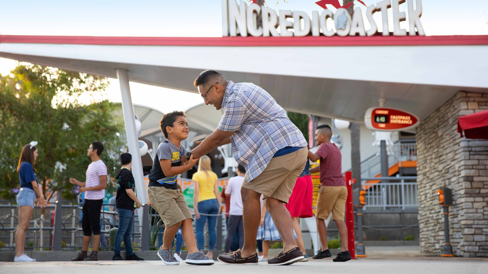 A parent and child interact playfully next to the line for Incredicoaster