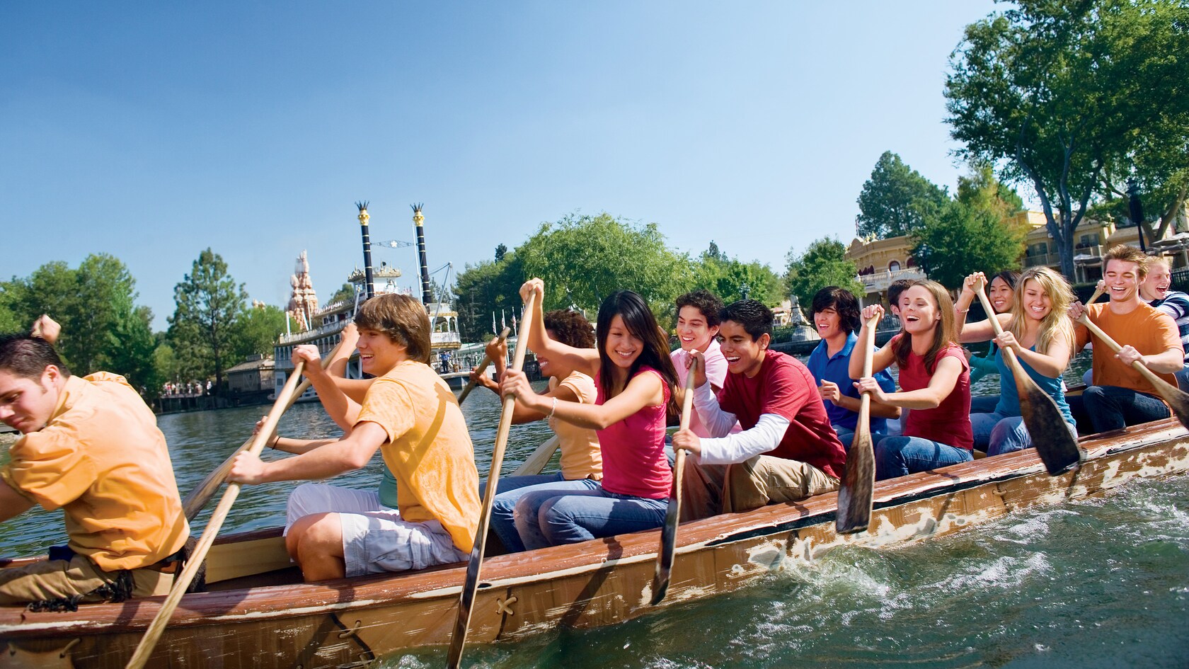 About 20 Happy Guests paddling a canoe with the Mark Twain Riverboat in the background