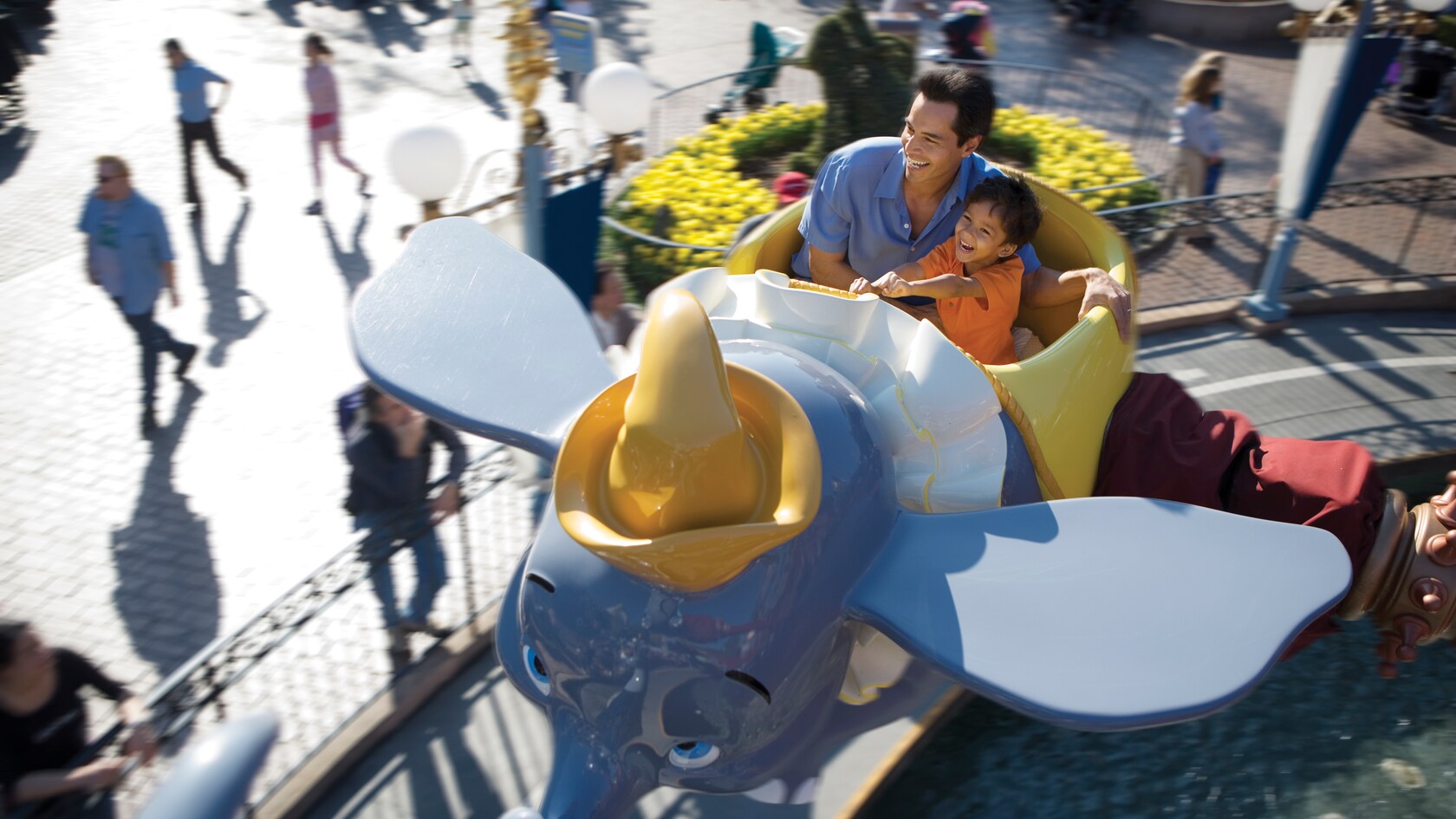 Un padre sonriente y su pequeño hijo disfrutan juntos la atracción Dumbo the Flying Elephant