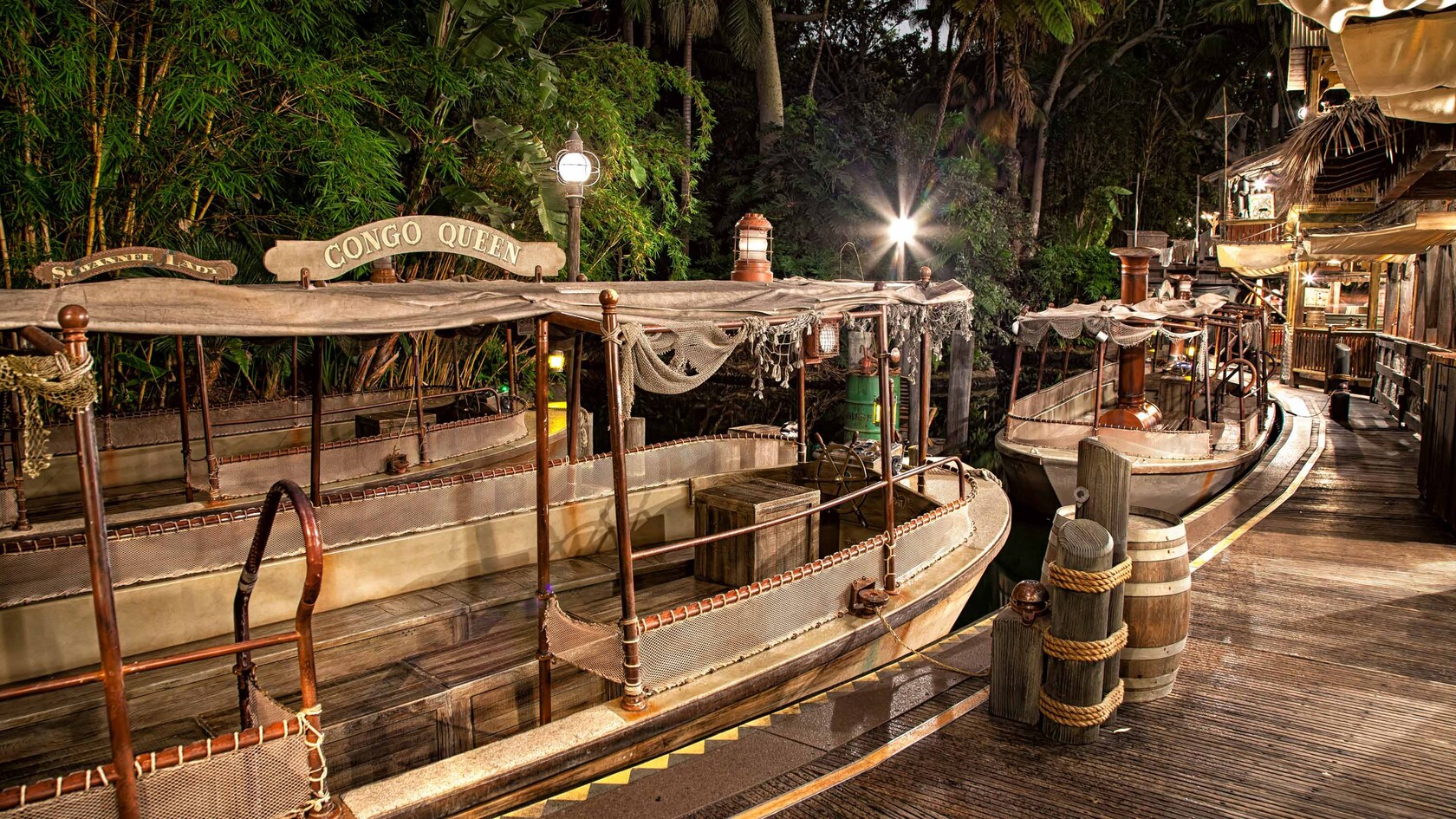 The Congo Queen, a wooden riverboat, moored to a pier with a jungle and huts