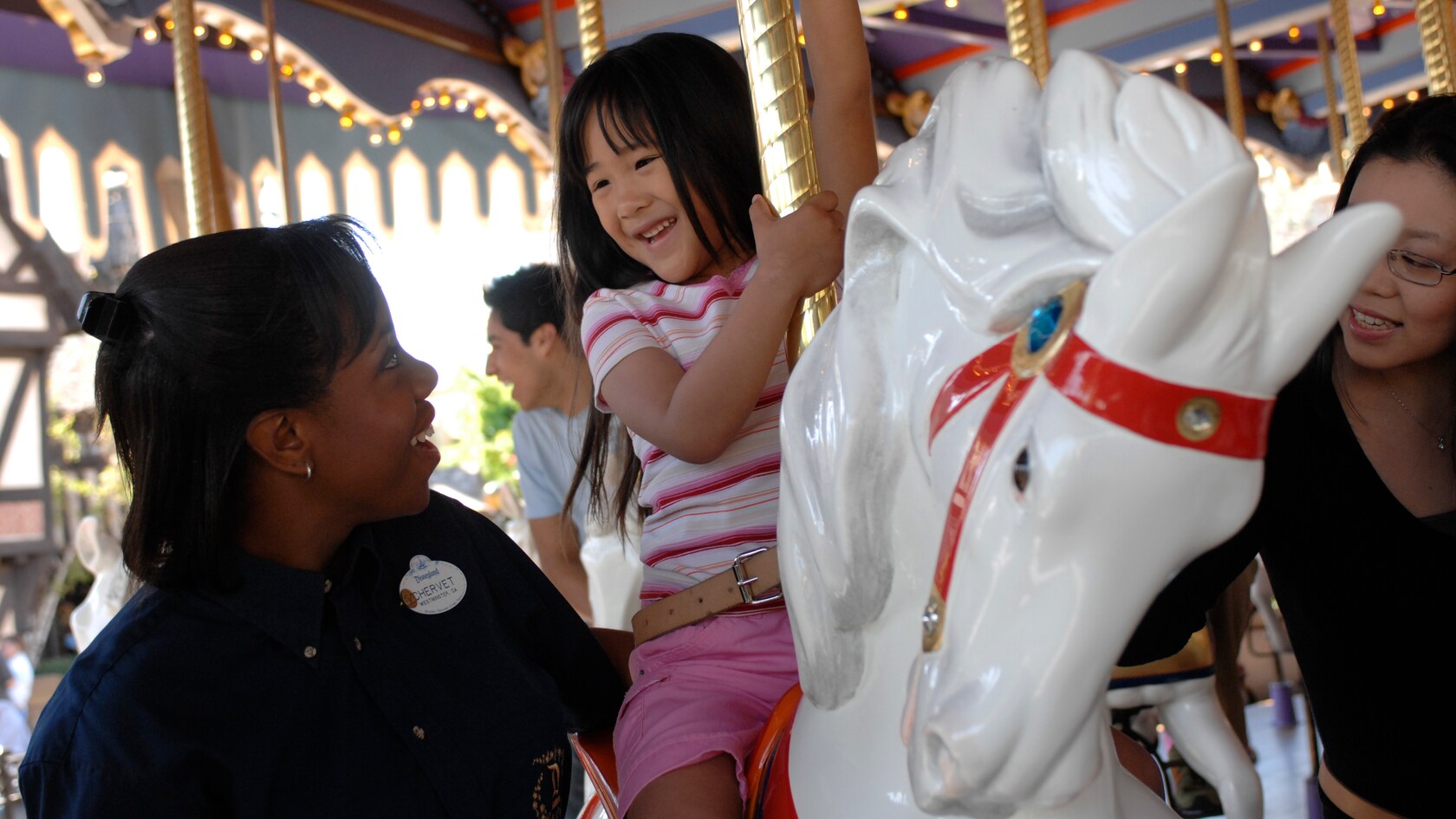A Cast Member makes sure a young Guest is secure on a horse aboard King Arthur's Carrousel