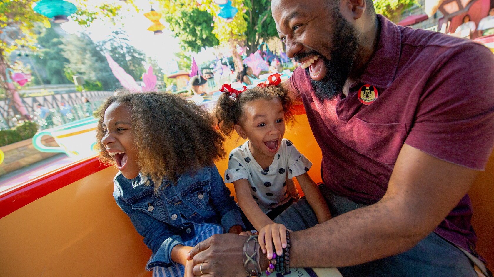 A dad and his 2 young daughters laugh while riding the Mad Tea Party attraction