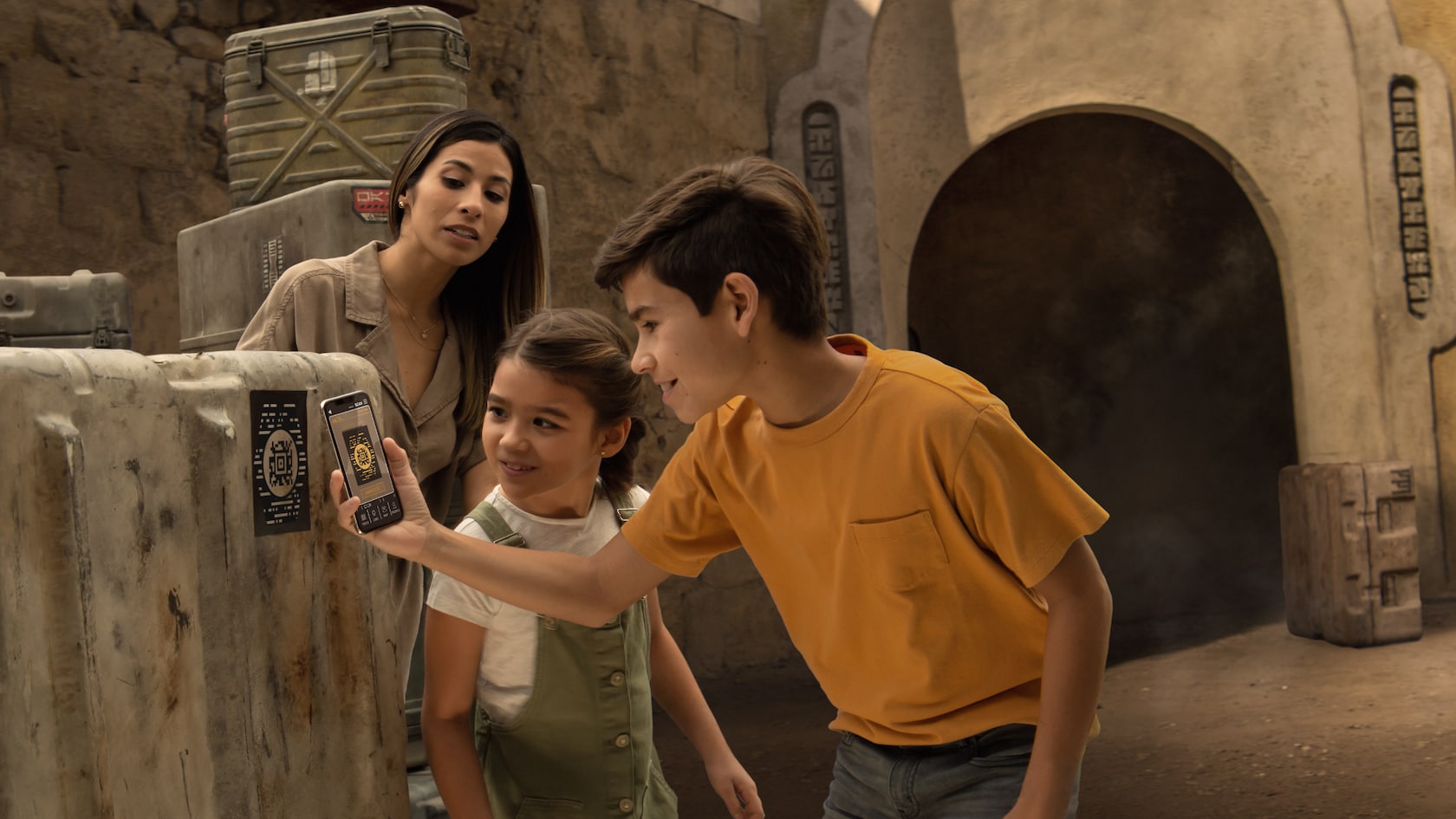 Un niño escanea un panel con su teléfono en Star Wars: Galaxy’s Edge mientras su madre y su hermana pequeña miran
