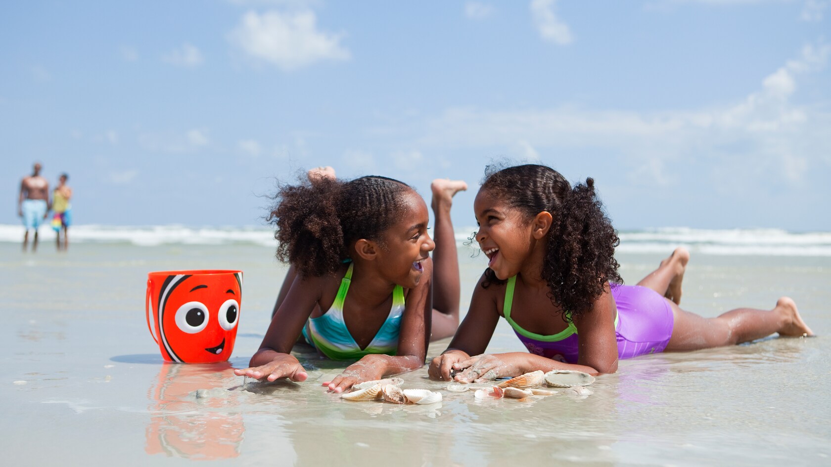 Two laughing girls lie on their stomachs in the wet sand at the beach