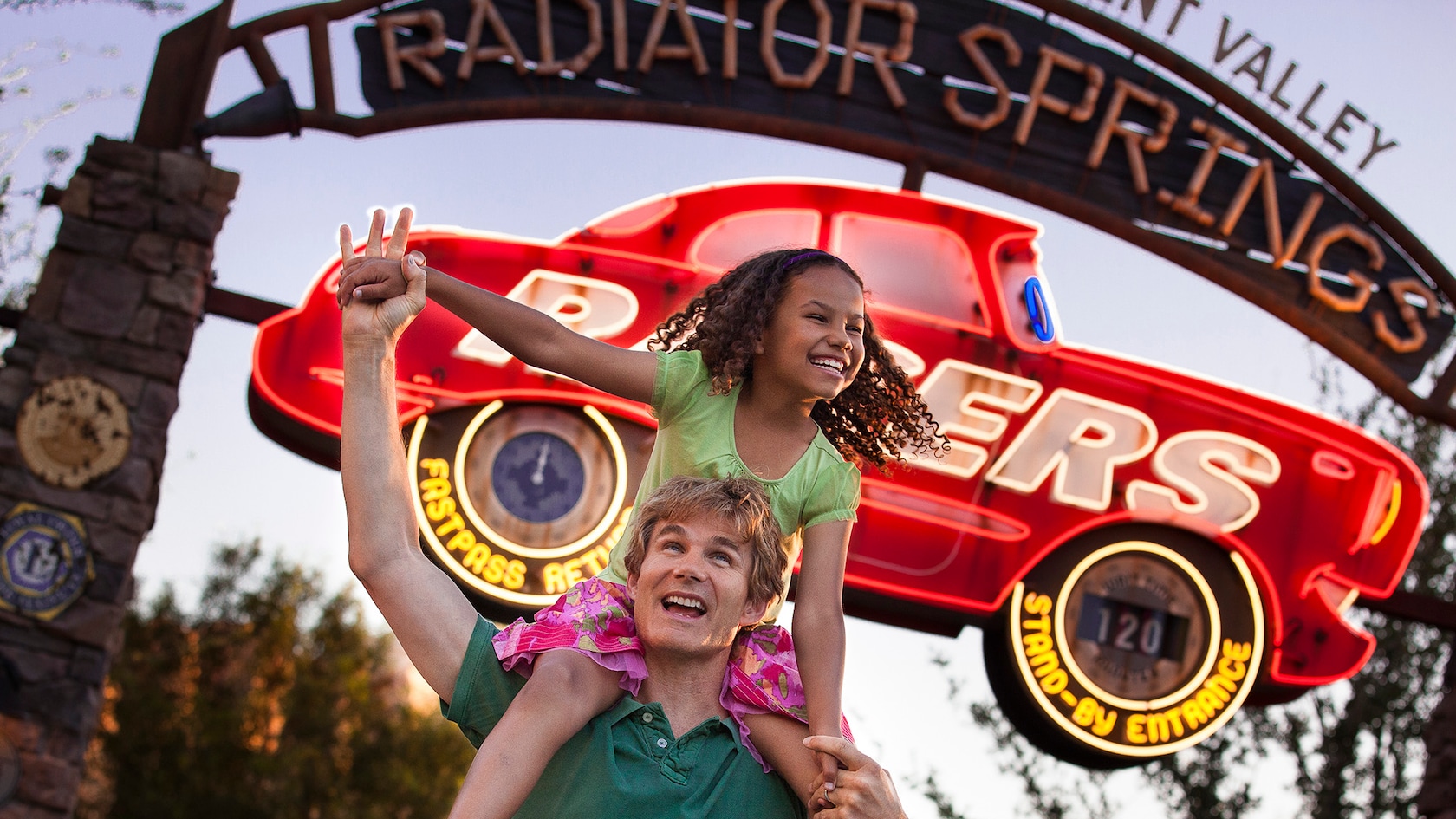 A girl sits on her dad's shoulder beneath a sign for Radiator Springs Racers in Cars Land