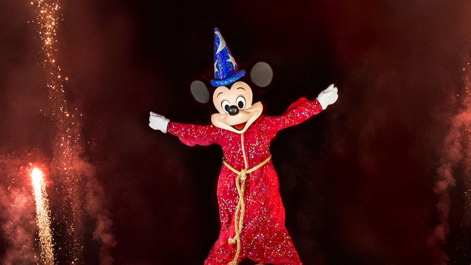 Sorcerer Mickey smiling while sparks fly through the evening sky during a performance of Fantasmic!