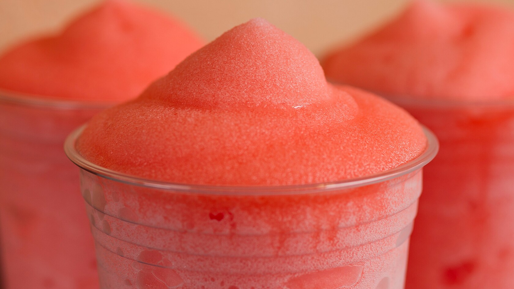 Three cups of icy cold frozen lemonade are topped with a swirl