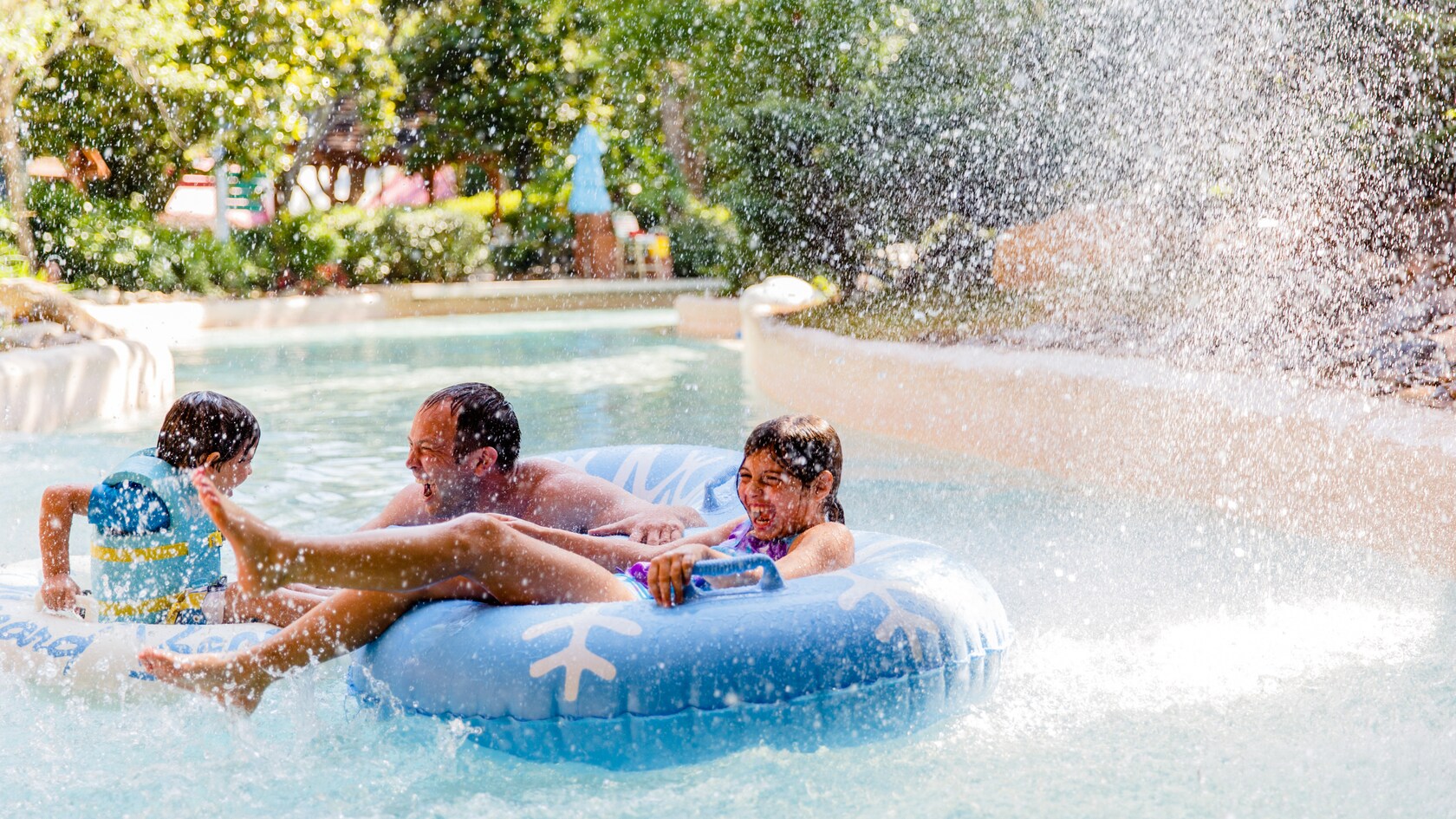 A father and his 2 kids scream with joy as water sprays them while they're floating on the creek