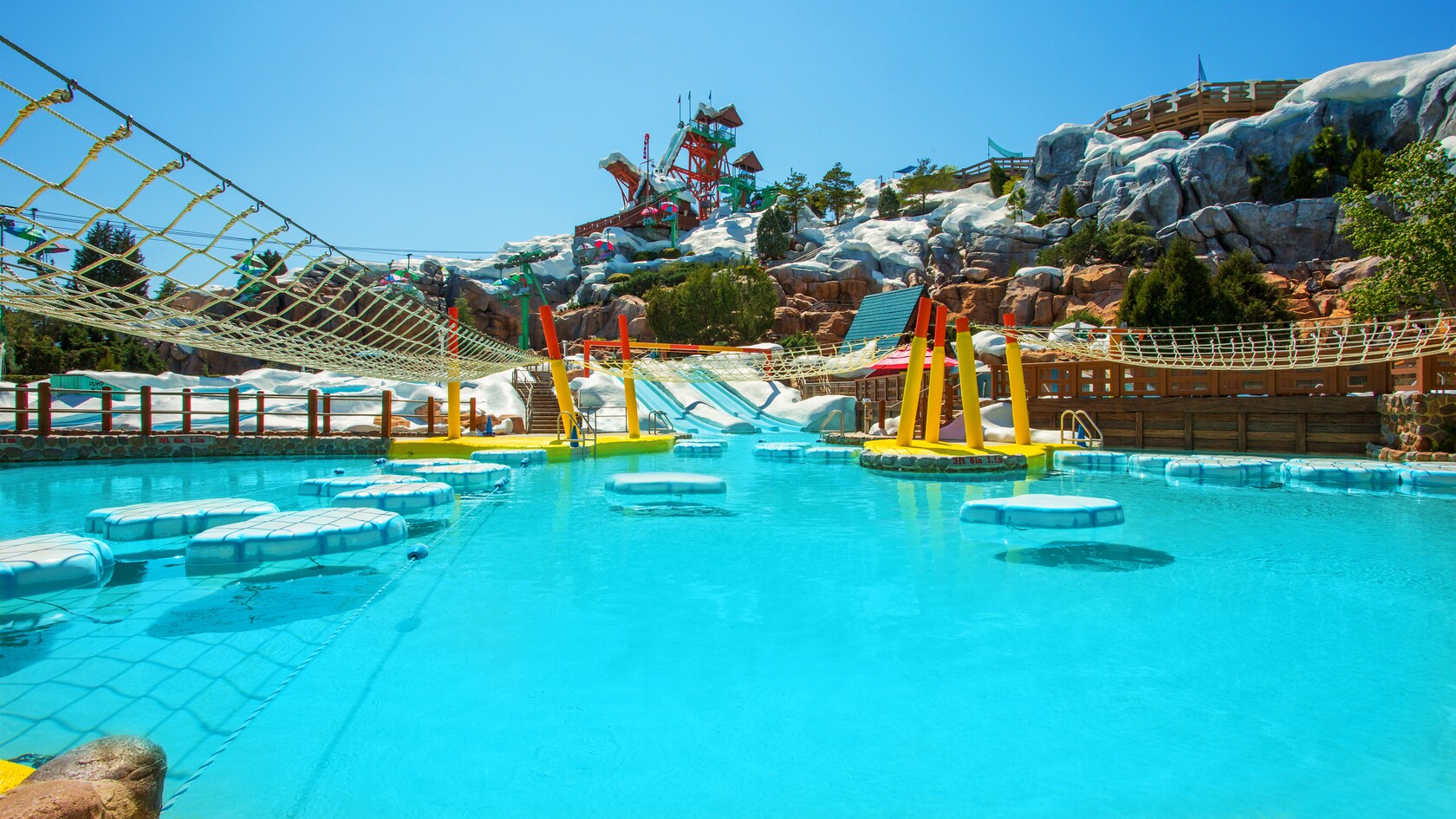 A pool with 3 sets of ice flows and cargo nets with Summit Plummet in the background