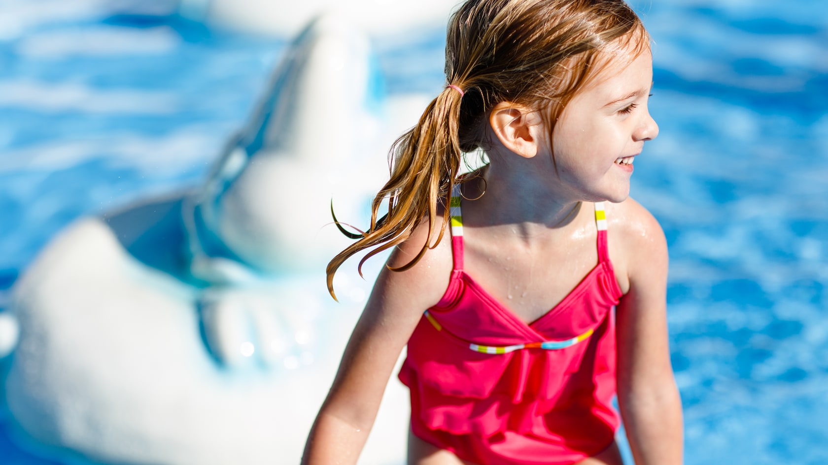 A smiling little girl stands in water near an ice sculpture