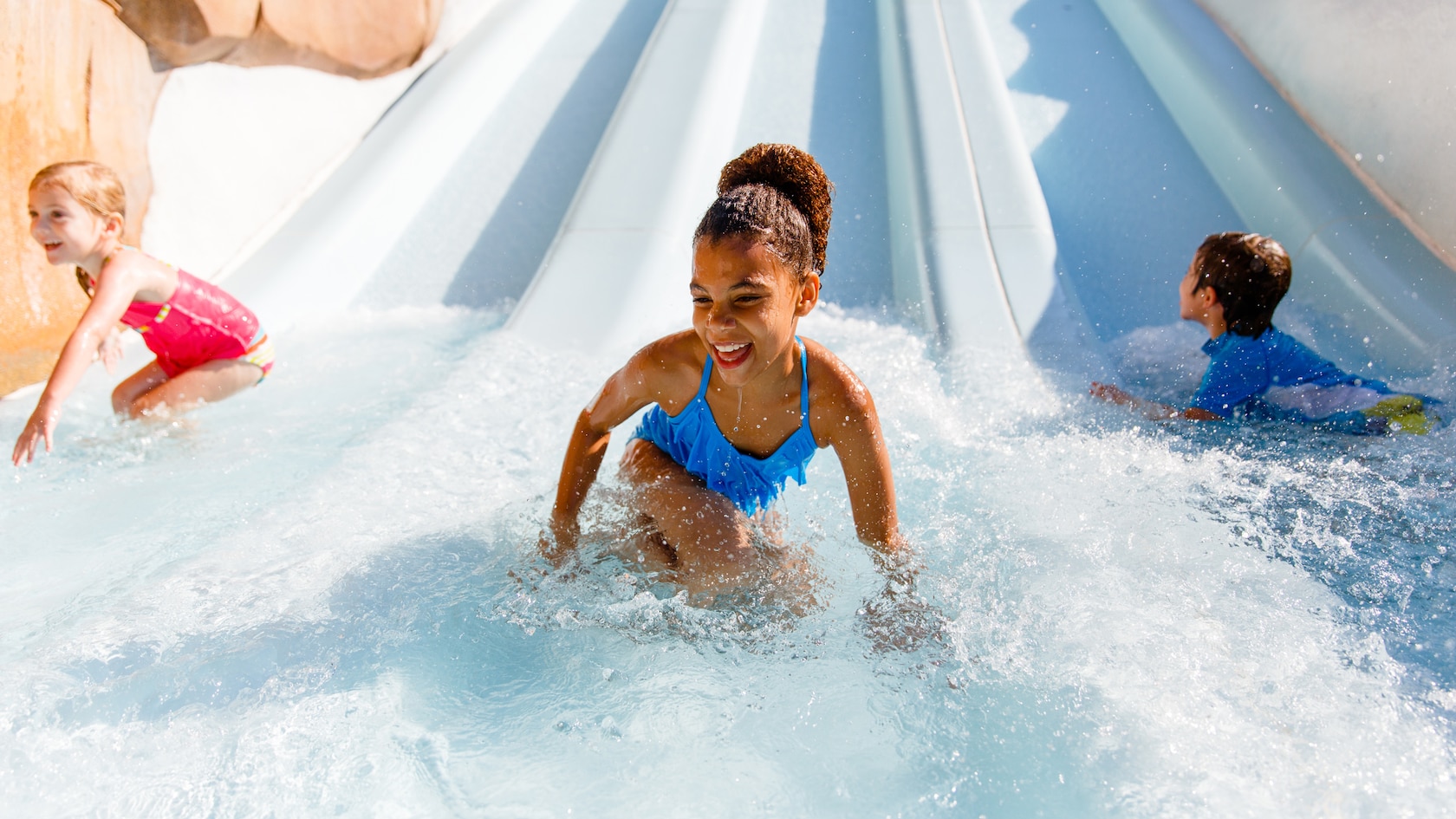 Three preschool-aged kids stand up after gliding down 3 side-by-side waterslides