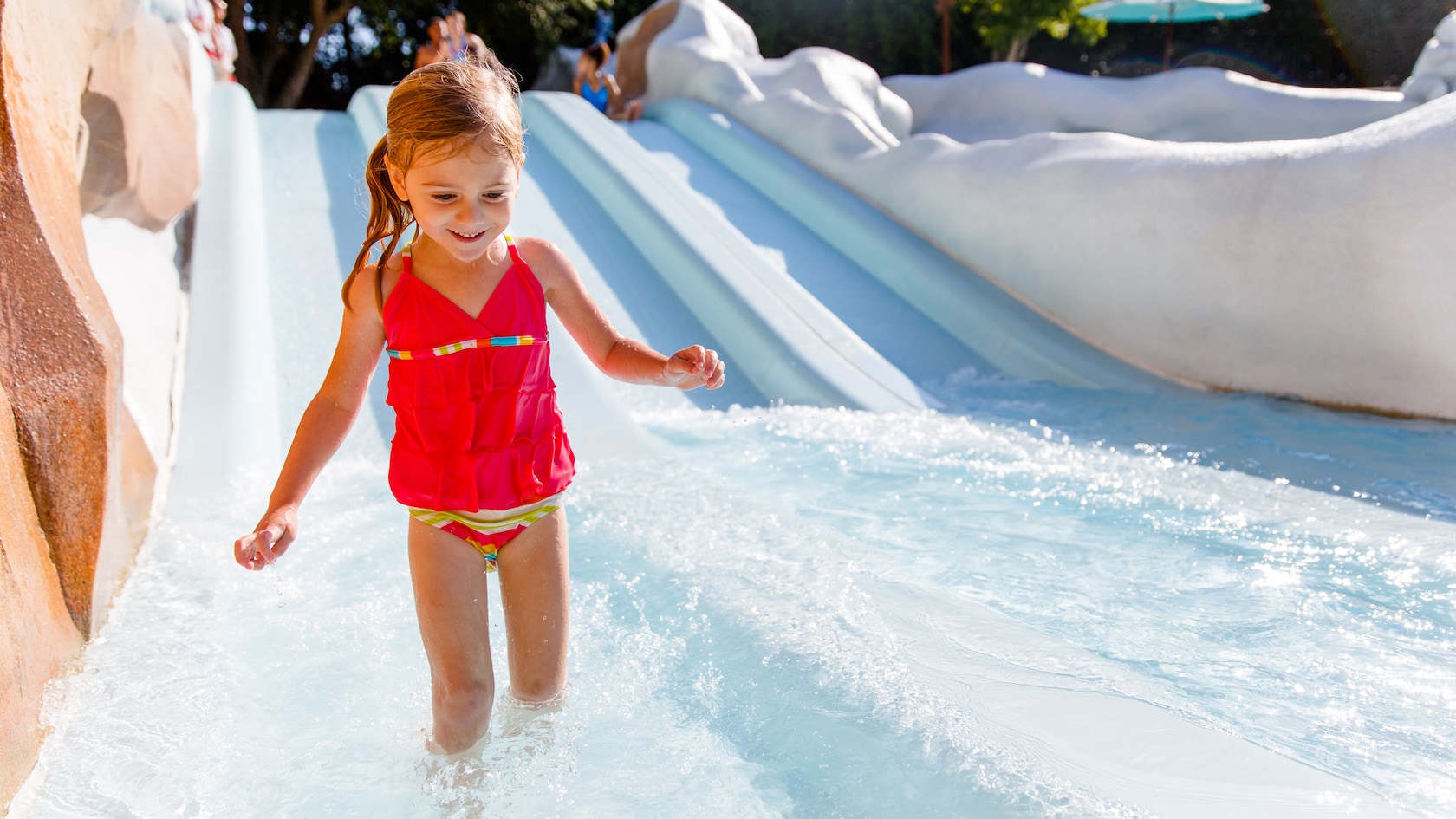 A preschool-aged girl walks in knee-high water at the end of the small waterslides