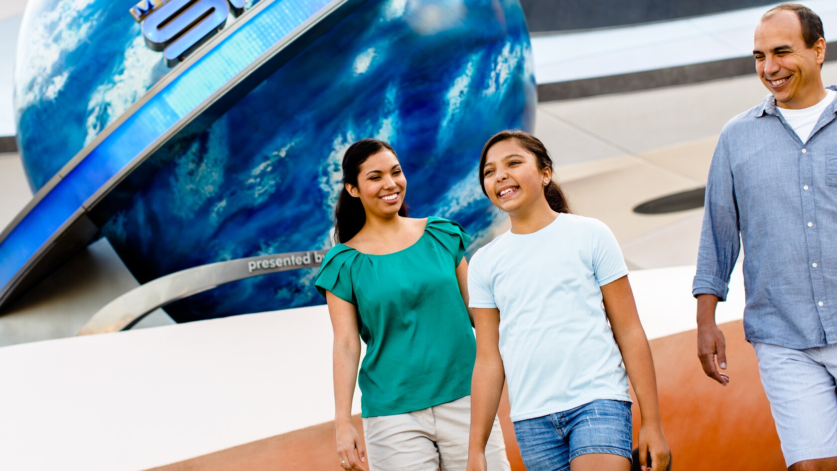Una familia de 3 personas camina cerca de la entrada a Mission: SPACE en EPCOT