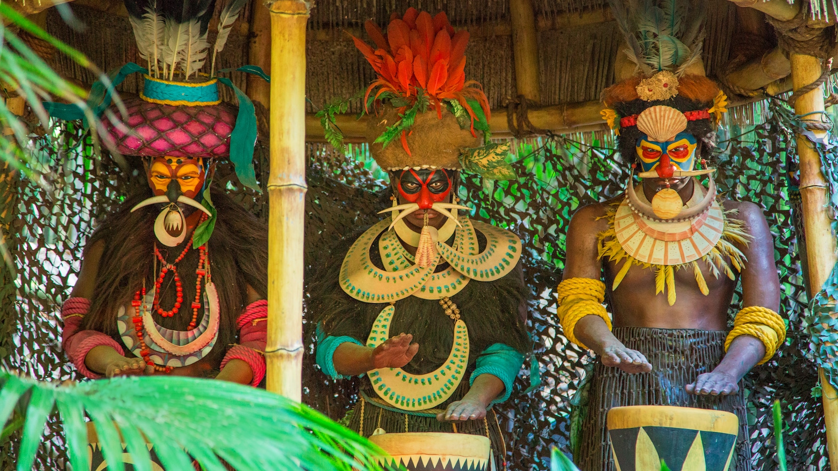 Three African headhunters, wearing war paint and traditional gear, play hand drums