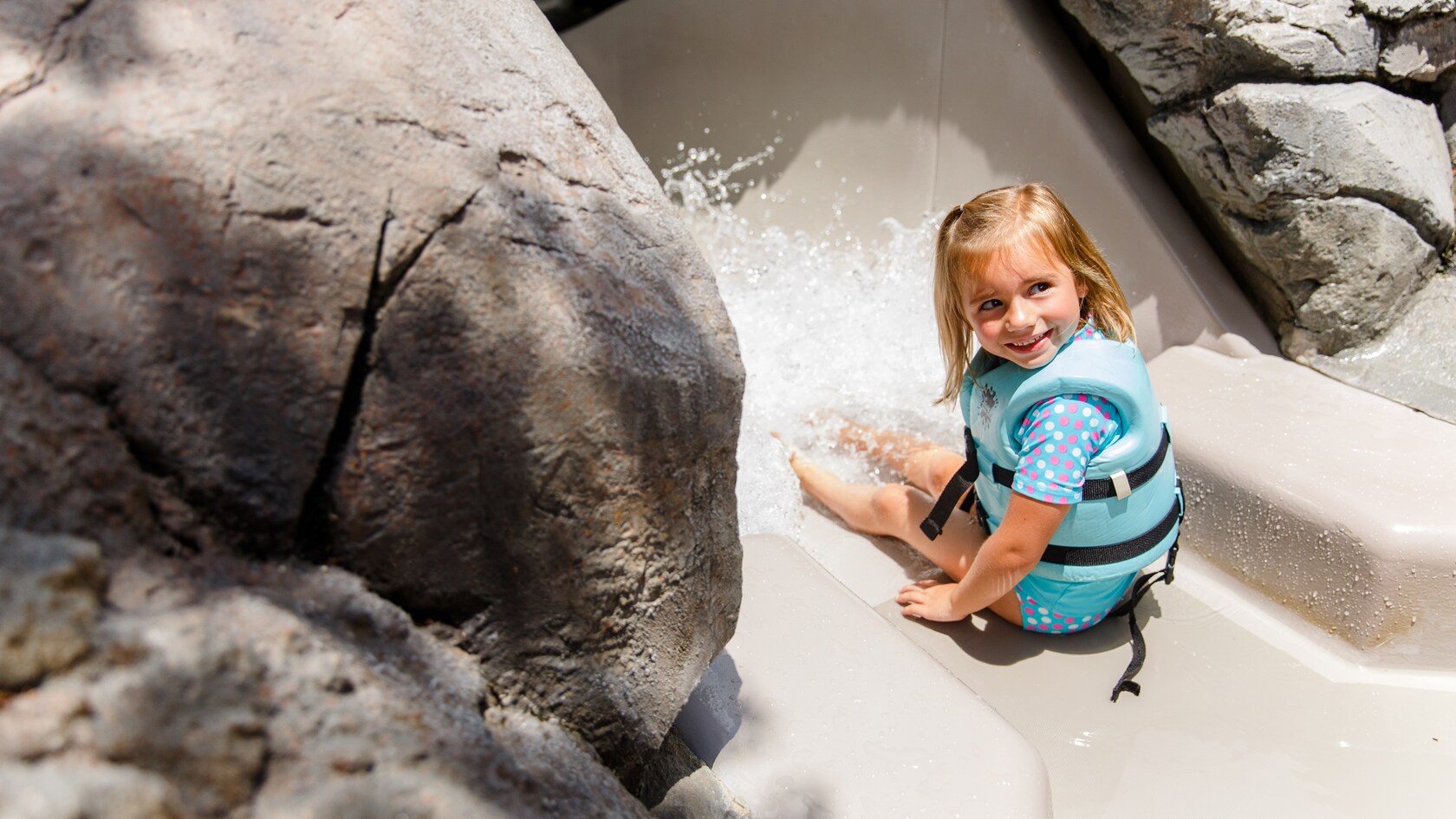 Une petite fille portant un gilet de sauvetage assise en haut d’une glissade d’eau aux Bay Slides