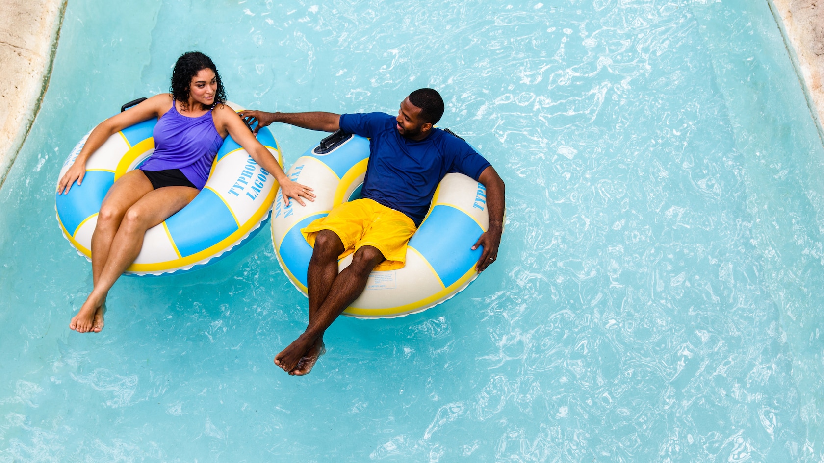 A man and a woman, in separate inner tubes, hold hands as they float down Castaway Creek