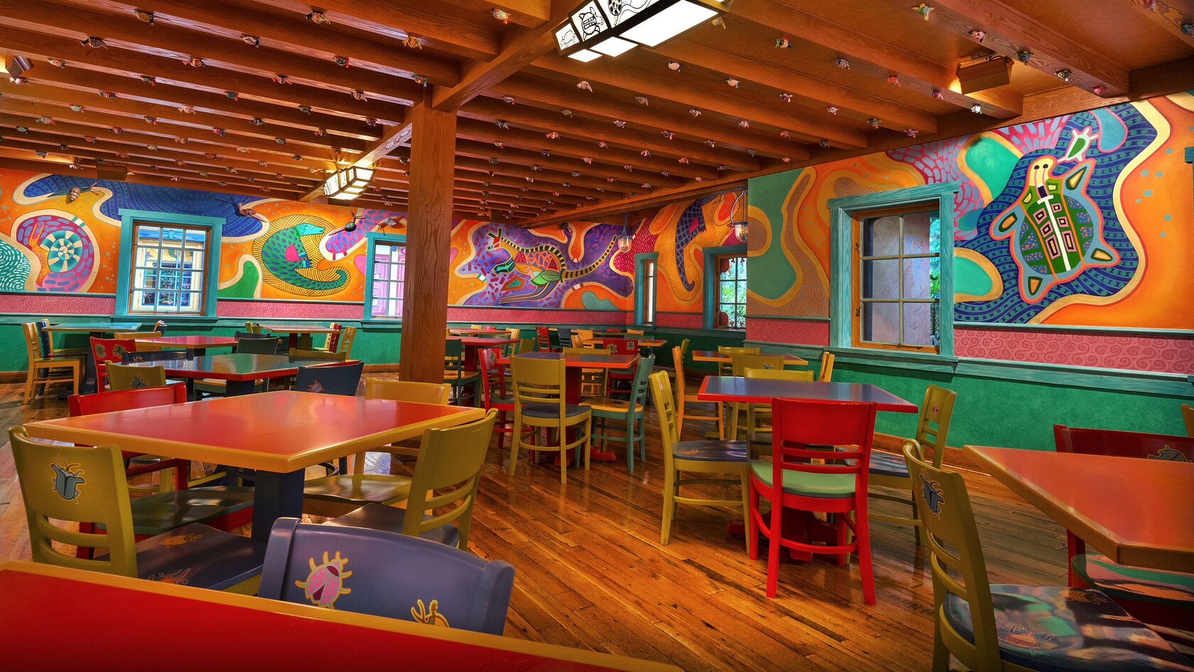 Mesas cuadradas coloridas junto a murales de animales estilizados