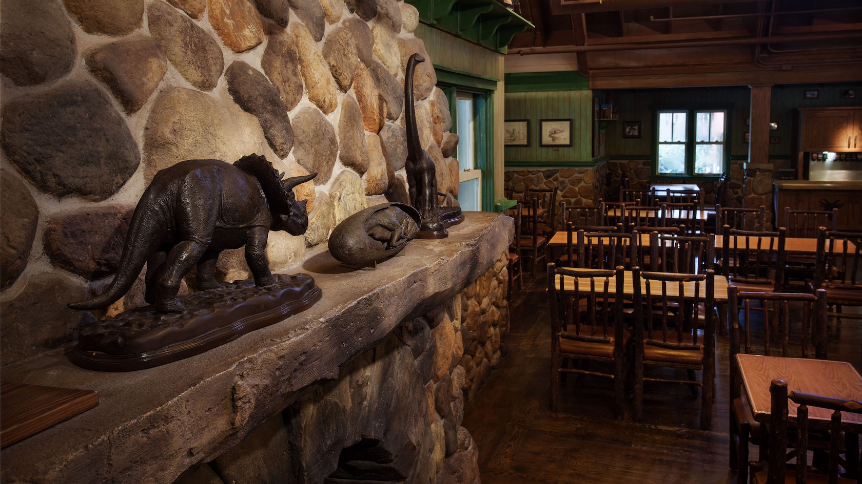 Stone fireplace with dinosaur statues on mantle next to tables and chairs