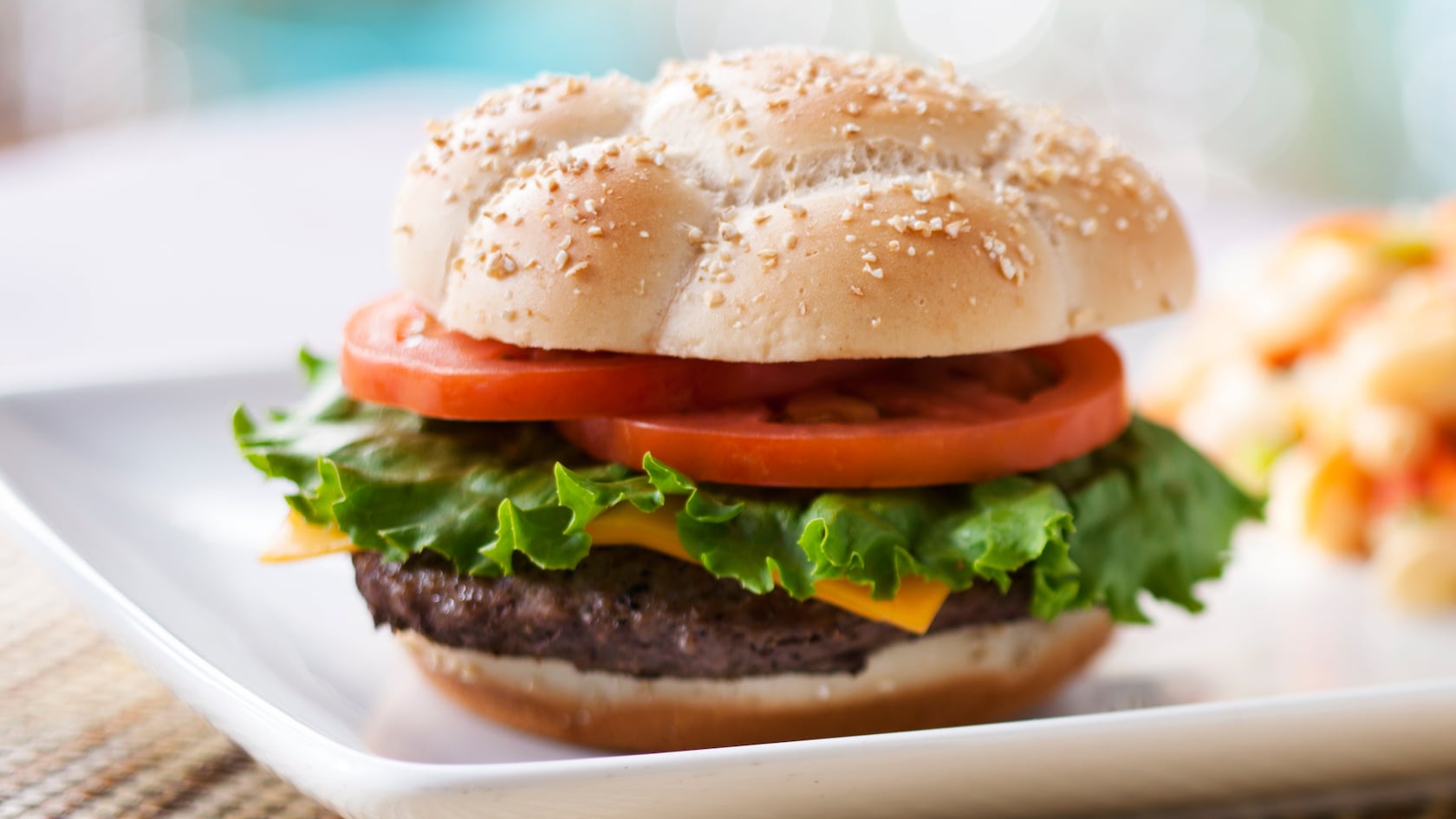 A juicy cheeseburger served with on a sesame seed bun with tomato slices and leaves of lettuce