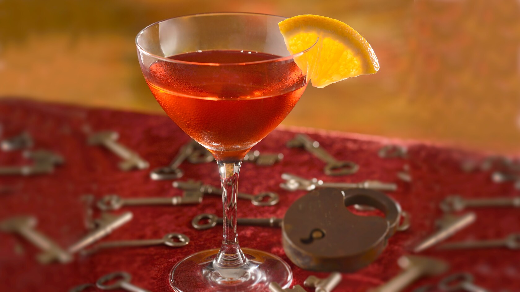 A negroni in a glass with a lemon garnish, set atop a table decorated by a lock and assorted keys