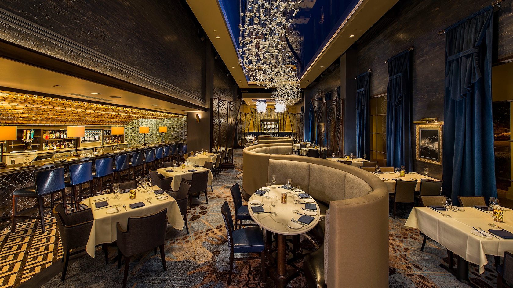 Under ambient lighting, rows of expertly set tables line the dining section near a full service bar