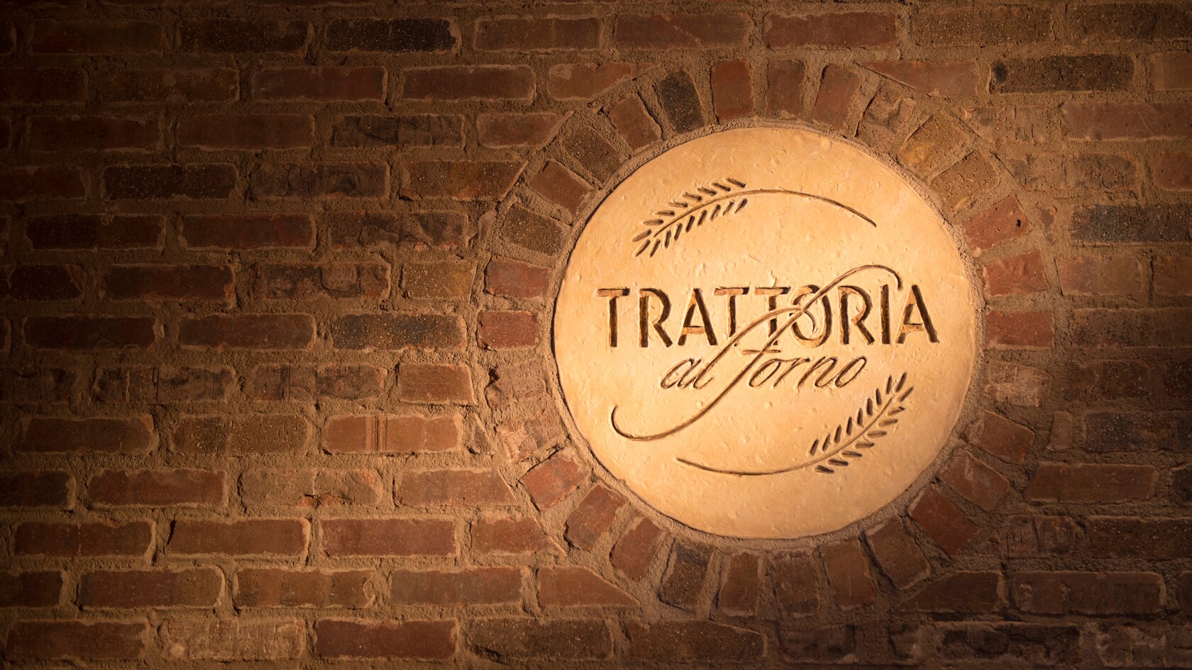 O logo do restaurante Trattoria al Forno em relevo em um círculo de estuque e emoldurado por alvenaria rústica.
